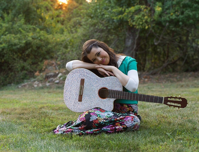 Shaindel sitting outdoors with her guitar